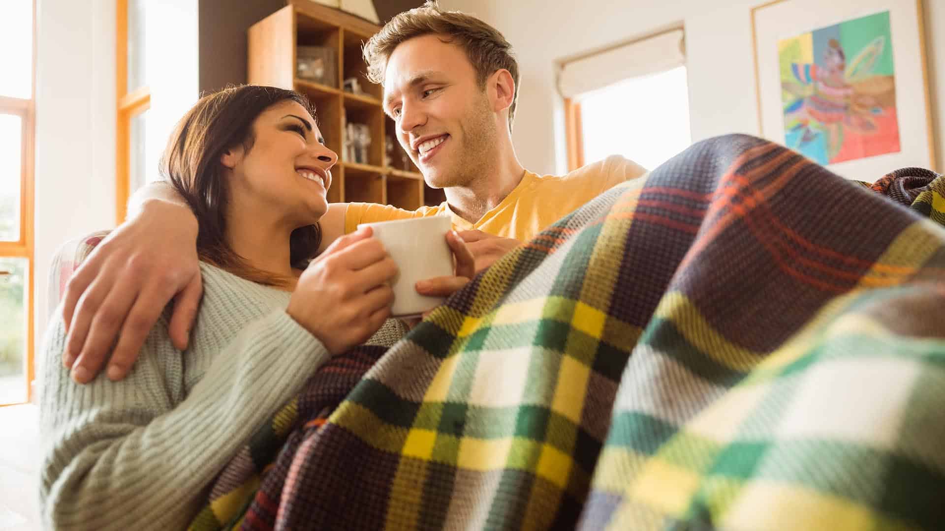 Young couple cuddling on the couch under blanket at home in the living room