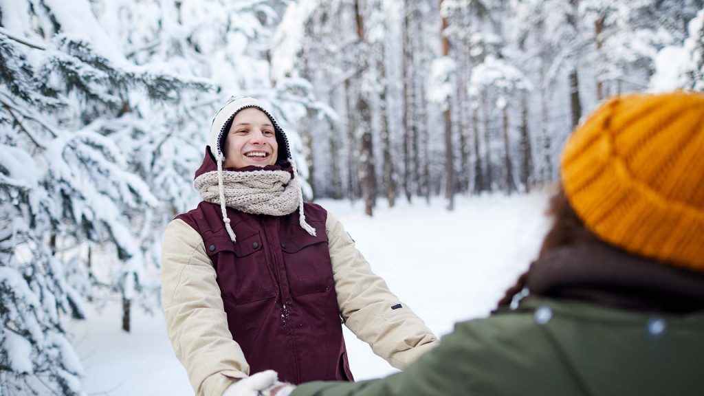 Portrait of playful young couple having fun outdoors in winter and holding hands, copy space