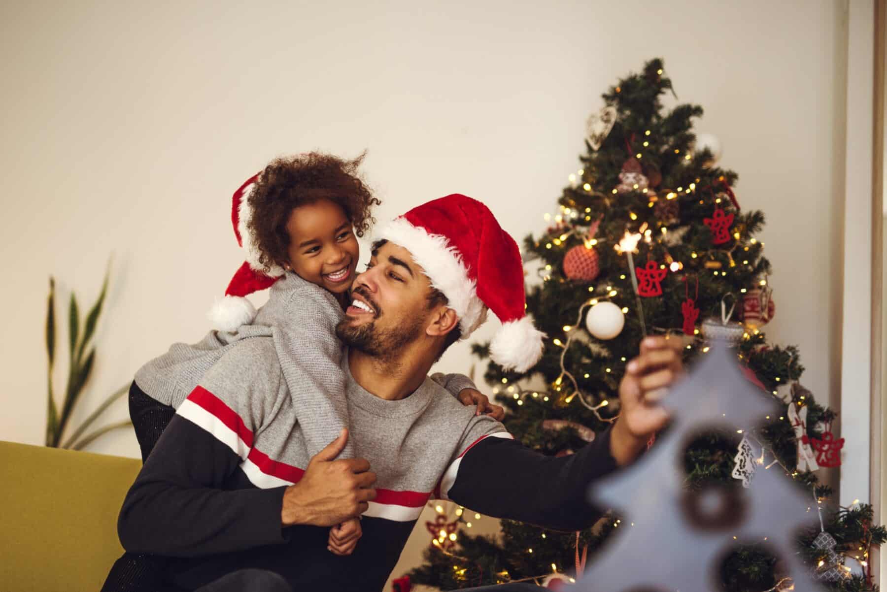 Cute african american girl decorating Christmas tree with dad.