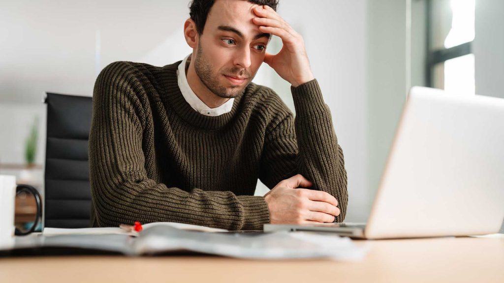 Stressed business man looking at laptop while sitting at the office desk