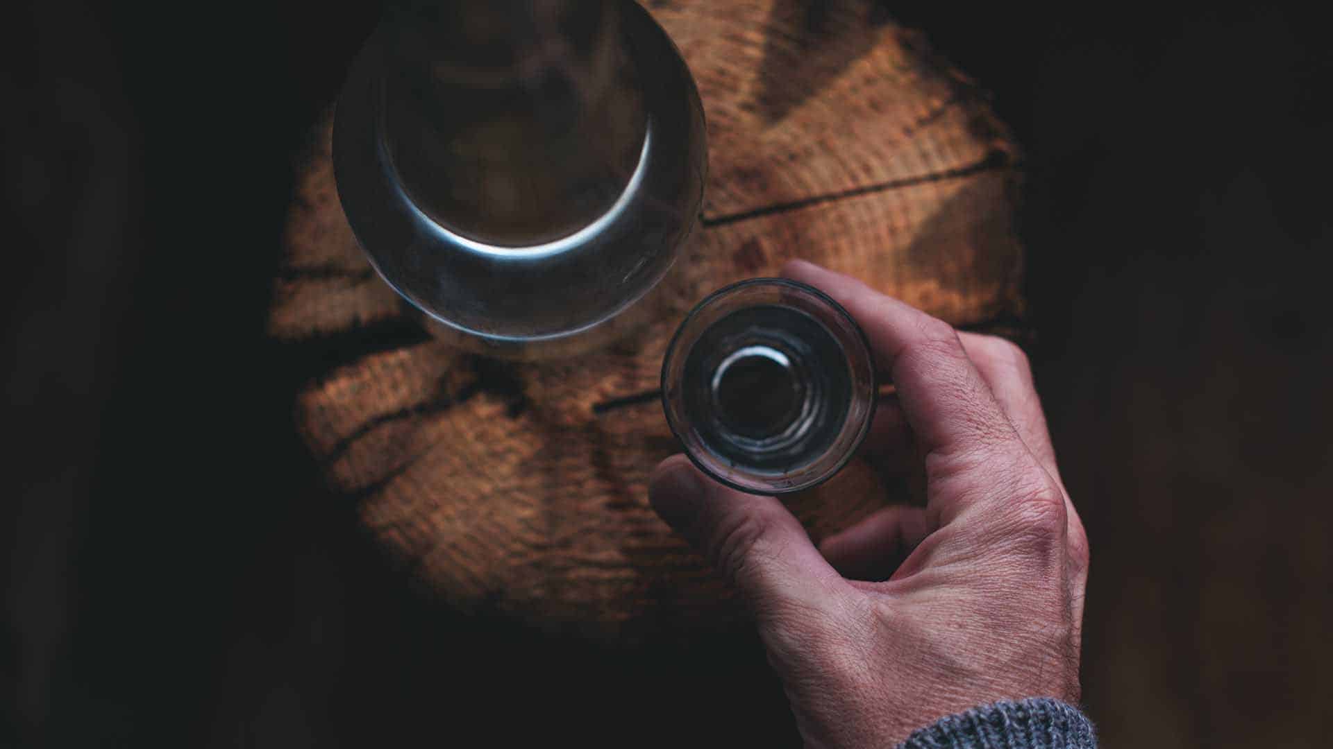 Man drinking strong alcohol drink from a shot glass, close up of hand, overhead view with selective focus