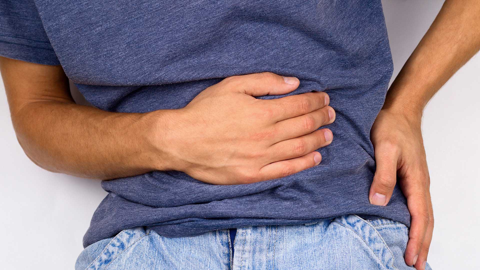 young man in jeans and t-shirt holds hands to his stomach and back, hernia or sports back injury concept