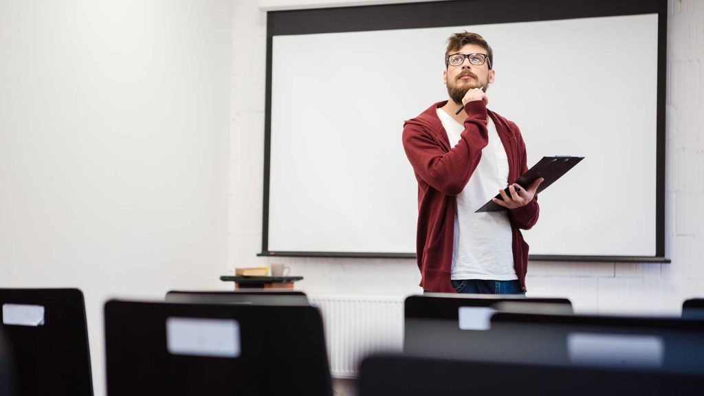 Young modern teacher with beard preparing for the lecture in classroom