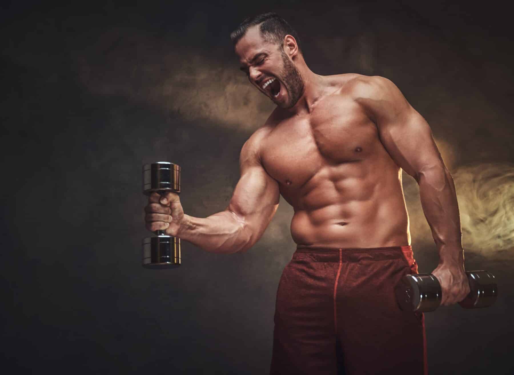 Young handsome bodybuilder is posing for photographer with dumbbells.